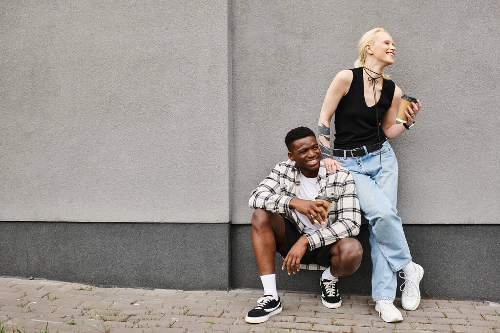 Um casal multicultural senta-se pacificamente ao lado um do outro no pavimento urbano, compartilhando um momento terno de união. - Foto, Imagem
