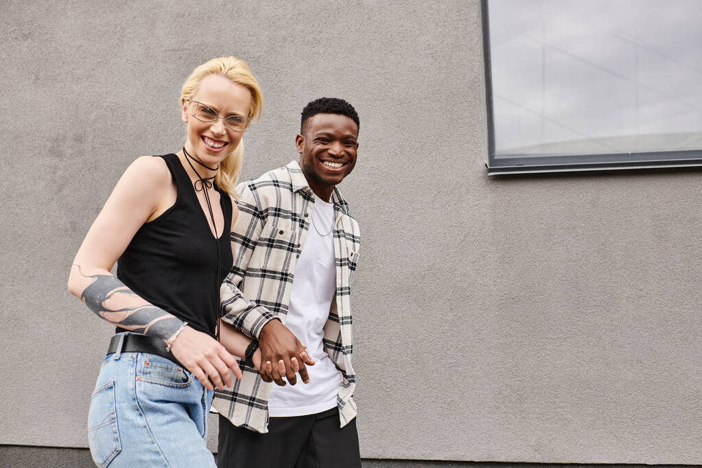 Egy boldog multikulturális pár, egy férfi és egy nő, együtt állnak egy városi utcában, egy szürke épület közelében.. - Fotó, kép