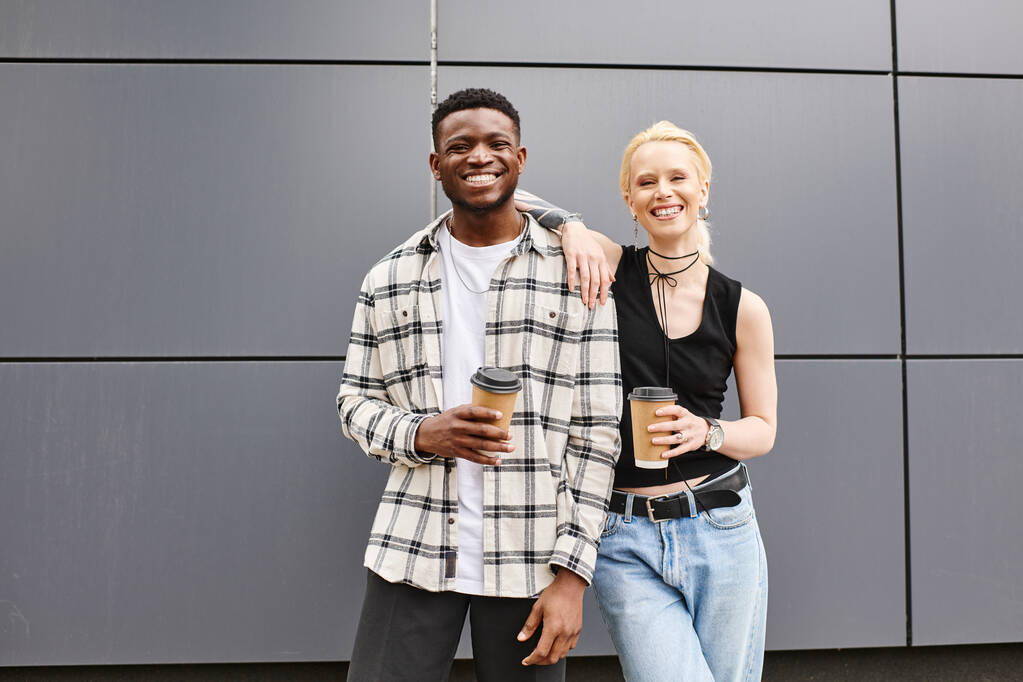 Um casal multicultural está feliz lado a lado em uma rua urbana perto de um edifício cinza. - Foto, Imagem