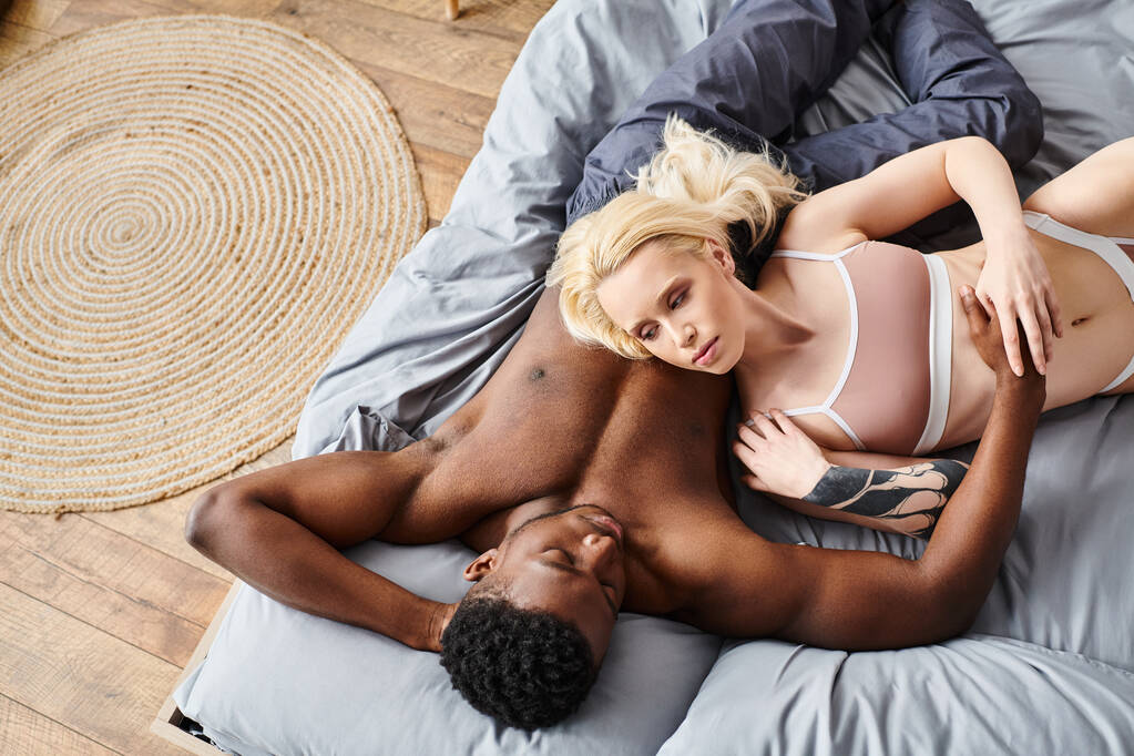 Egy multikulturális barát és barátnő romantikusan összefonódik egy ágyon otthon, megosztva egymással az intimitás pillanatát.. - Fotó, kép