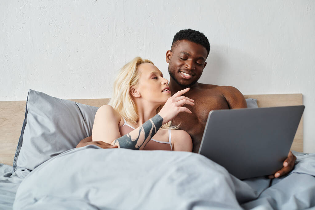 Çok kültürlü bir çift, dizüstü bilgisayarlarının içeriğine dalmış bir şekilde yatakta dinleniyor.. - Fotoğraf, Görsel