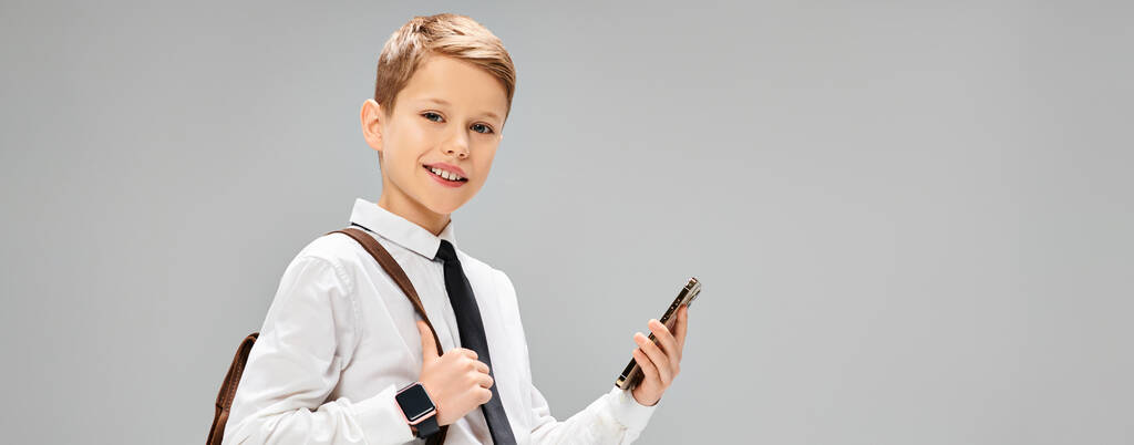 Εφηβικό αγόρι με λευκό πουκάμισο και γραβάτα κρατώντας ένα κινητό τηλέφωνο, απεικονίζοντας μια επιχειρηματική ιδέα. - Φωτογραφία, εικόνα