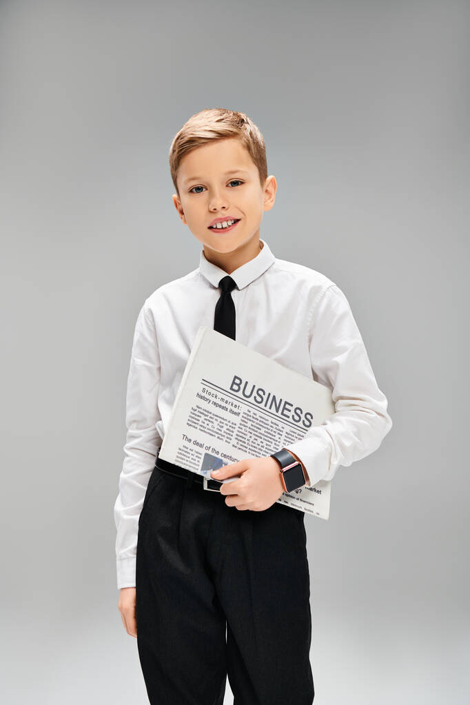 Mladý chlapec ve formálním oděvu drží noviny na šedém pozadí. - Fotografie, Obrázek