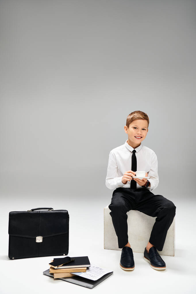 Un jeune garçon en tenue intelligente est assis à côté d'une mallette. - Photo, image