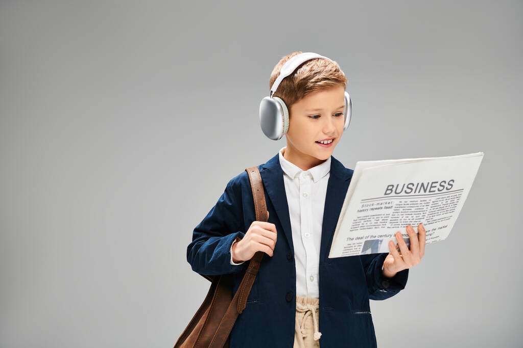 Niño con elegante atuendo lee el periódico mientras usa auriculares. - Foto, imagen
