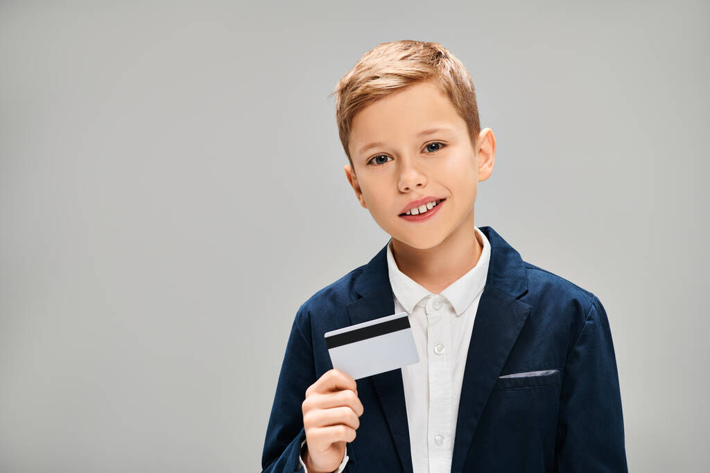 Εφηβικό αγόρι σε ένα κοφτερό κοστούμι με αυτοπεποίθηση κατέχει μια πιστωτική κάρτα. - Φωτογραφία, εικόνα