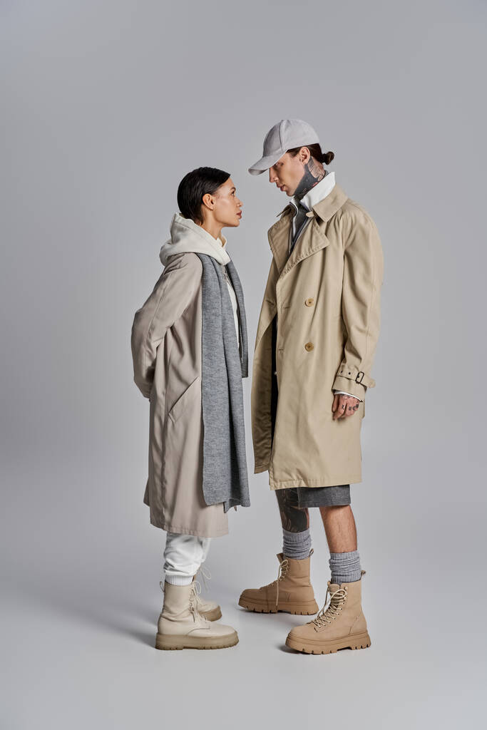 Paar stehen Seite an Seite in stylischen Trenchcoats und verströmen vor grauem Hintergrund eine raffinierte und modische Atmosphäre. - Foto, Bild