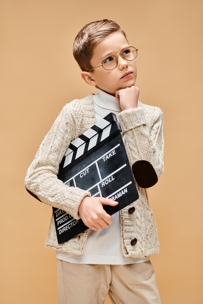 Jonge jongen in bril houdt film klapbord op beige achtergrond. - Foto, afbeelding