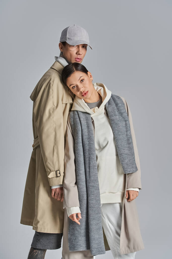 Ein junger Mann und eine junge Frau stehen elegant nebeneinander in Trenchcoats und versprühen Stil und Raffinesse in einem Studioambiente. - Foto, Bild
