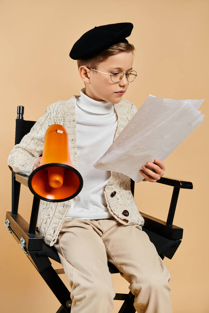 Serdülő fiú filmrendezőnek öltözve, kezében egy darab papírral, miközben egy székben ül.. - Fotó, kép