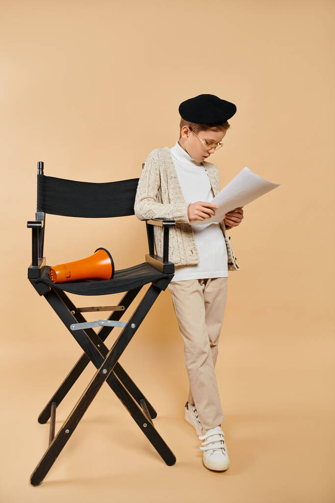 Film yönetmeni gibi giyinmiş, katlanan sandalyede gazete okuyan genç bir çocuk.. - Fotoğraf, Görsel