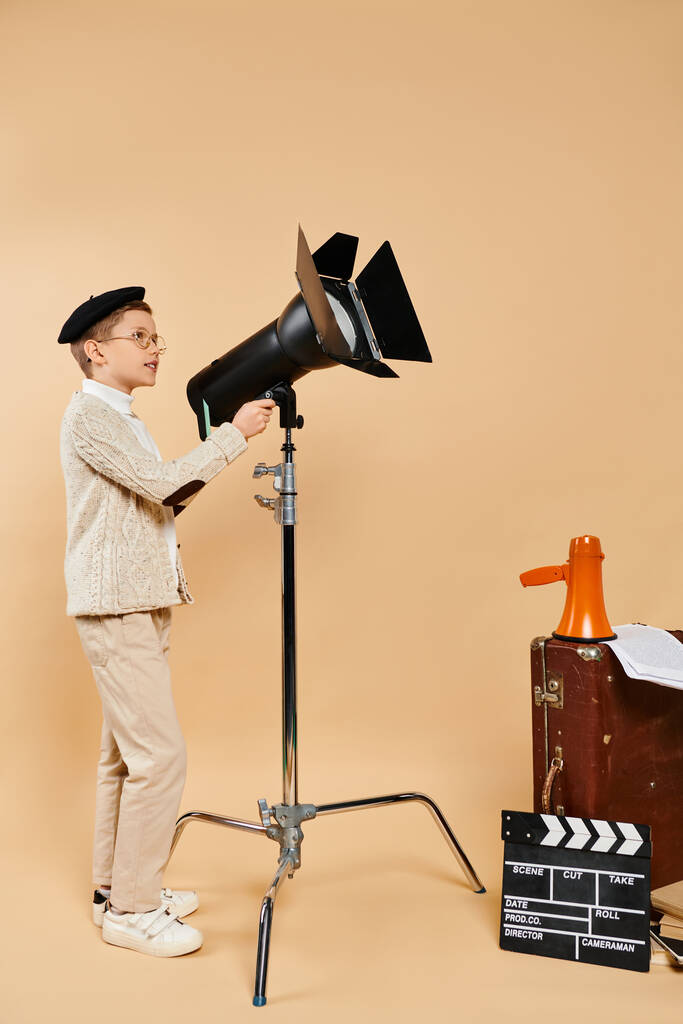 Предприимчивый мальчик уверенно стоит рядом с камерой и штативом. - Фото, изображение