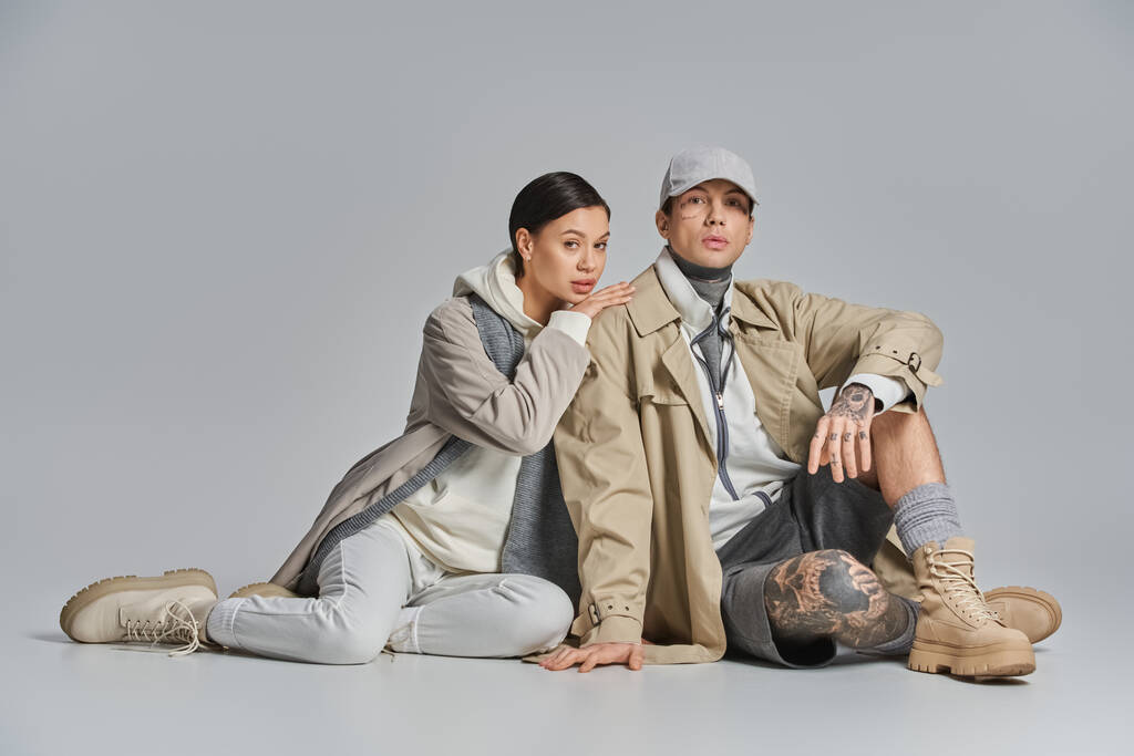 Un hombre y una joven mujer con estilo en una gabardina se sientan juntos en el suelo, compartiendo un momento de conexión e intimidad. - Foto, imagen