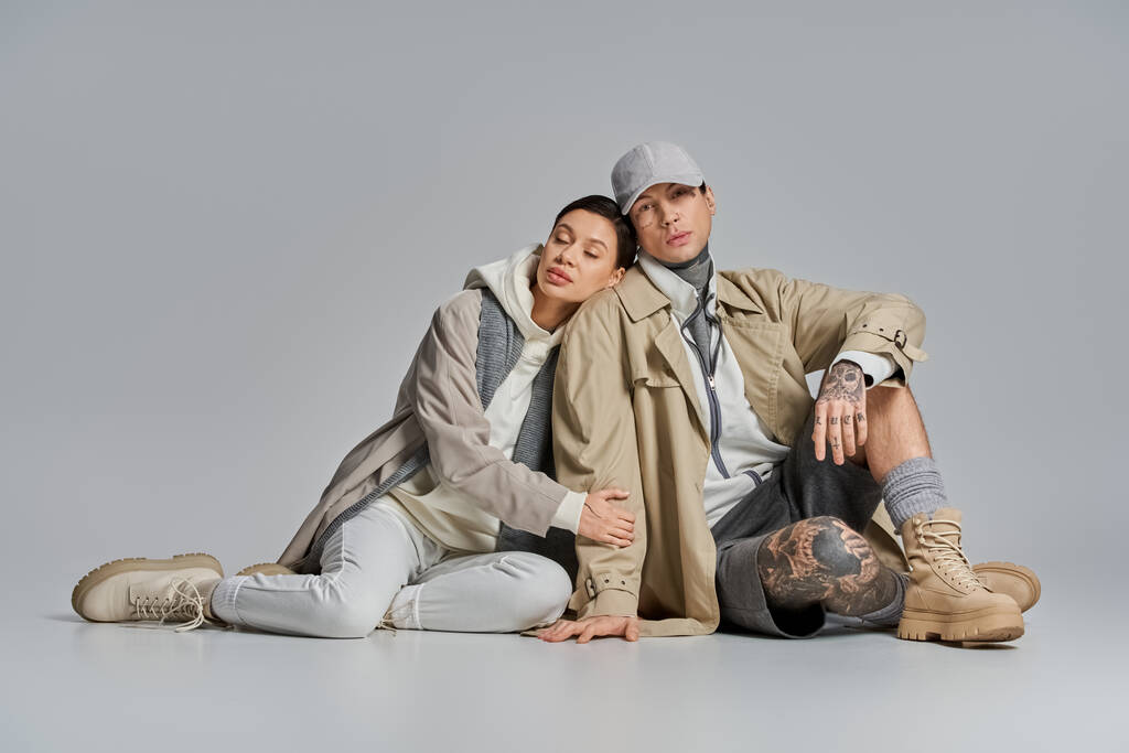Een stijlvolle jonge vrouw in een regenjas zittend op de grond met haar partner, genietend van een moment van saamhorigheid - Foto, afbeelding