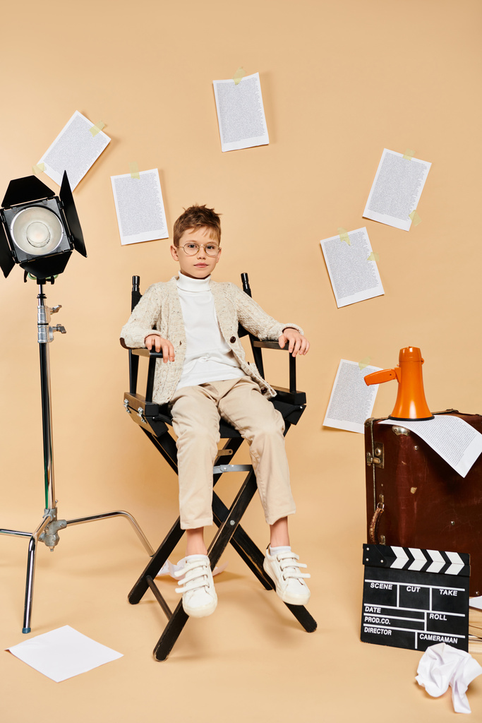 Młody chłopiec ubrany jak reżyser siedzący na krześle, gotowy do akcji. - Zdjęcie, obraz