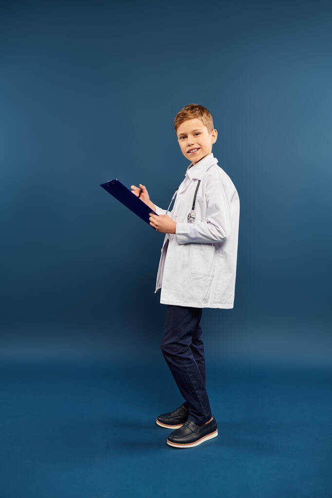 Un garçon préadolescent en blouse de laboratoire tenant un presse-papiers. - Photo, image