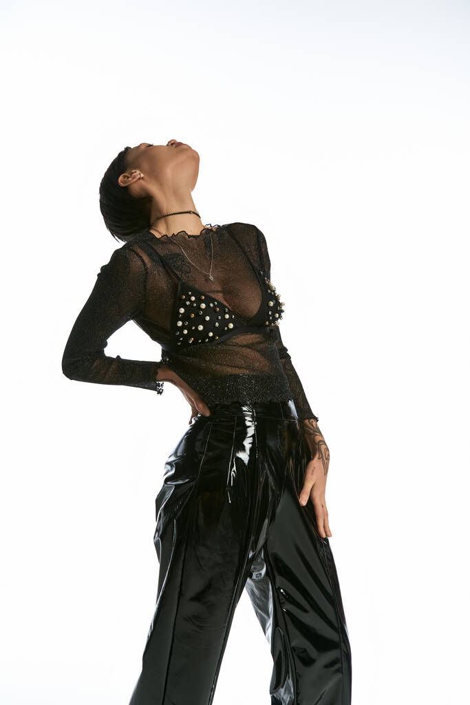 Egy nő fekete nadrágban és tiszta felsőben pózol egy szürke hátterű stúdióban, ragyogó stílusban és eleganciával.. - Fotó, kép