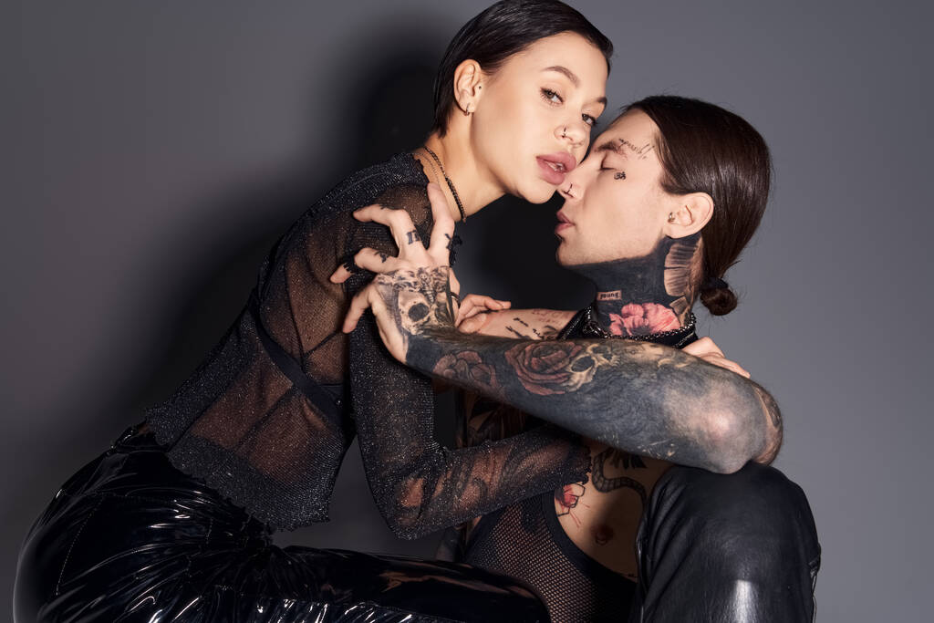 Deux jeunes femmes élégantes avec des tatouages assis étroitement ensemble dans un studio sur un fond gris. - Photo, image