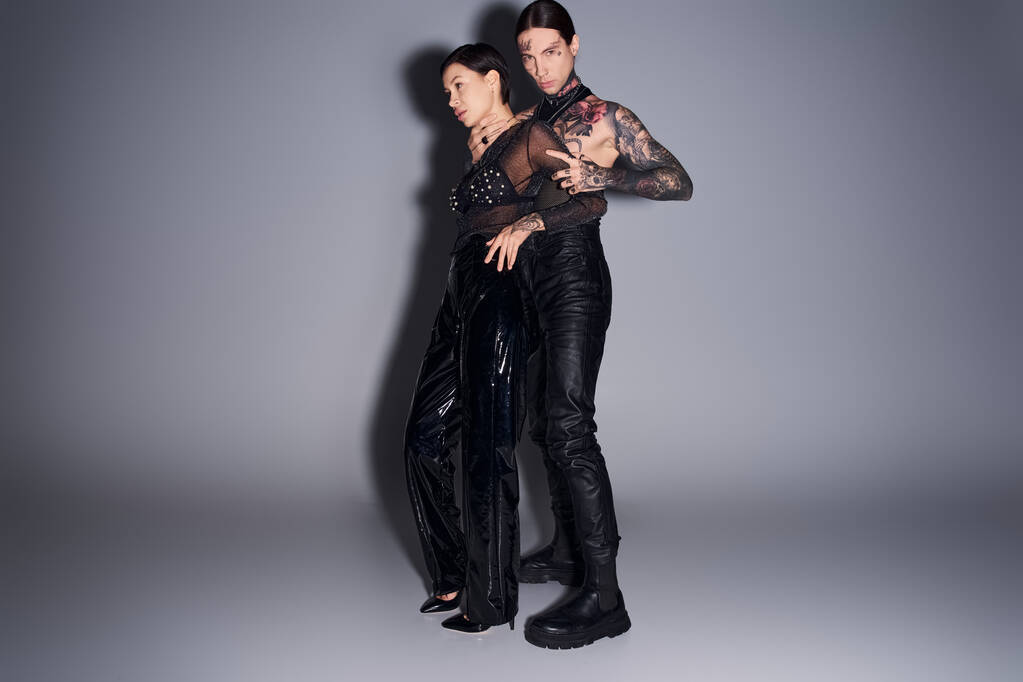 Um jovem, elegante e tatuado casal de pé juntos em um estúdio contra um fundo cinza. - Foto, Imagem