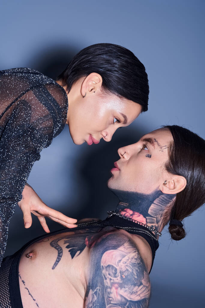 Two young women, stylish and tattooed, stand side by side in a studio against a grey background, exuding confidence and connection. - Photo, Image