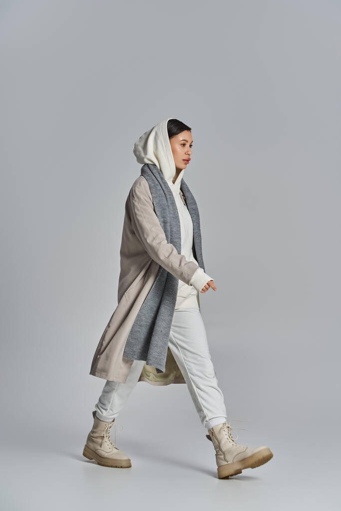 Une femme élégante marchant dans une tenue grise et blanche dans un cadre de studio. - Photo, image
