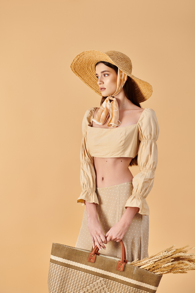 Uzun esmer saçlı genç bir kadın, şık bir şapka takarken elinde sepet tutan bir yaz elbisesi içinde huzurlu poz veriyor.. - Fotoğraf, Görsel