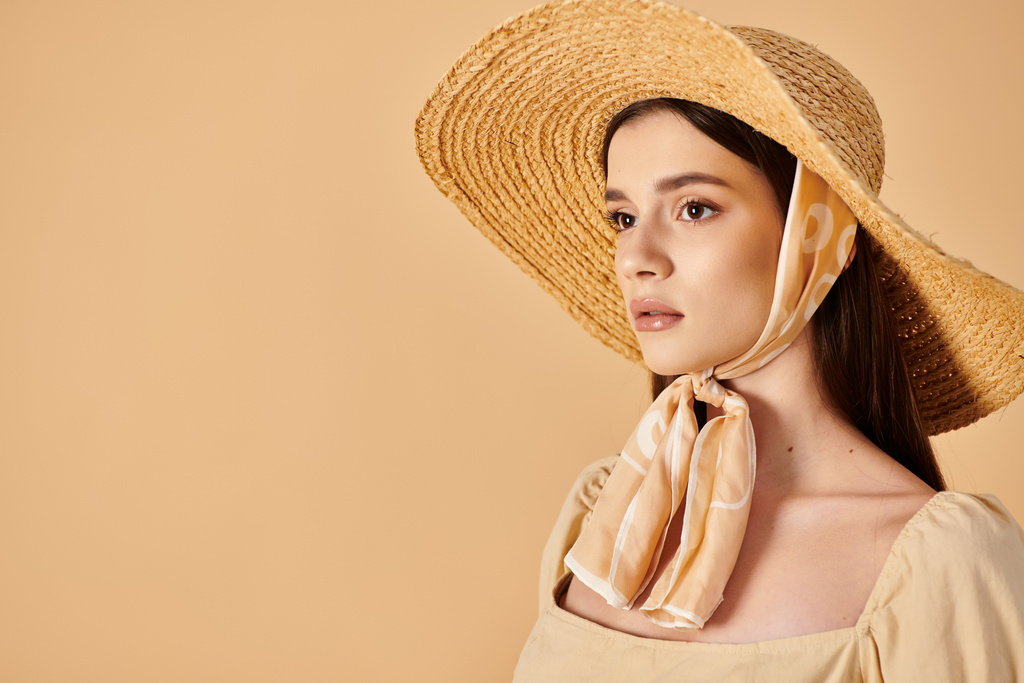 Una mujer joven con el pelo largo y morena posa en un traje de verano, con un sombrero de paja y bufanda, exudando un ambiente relajado de verano. - Foto, Imagen