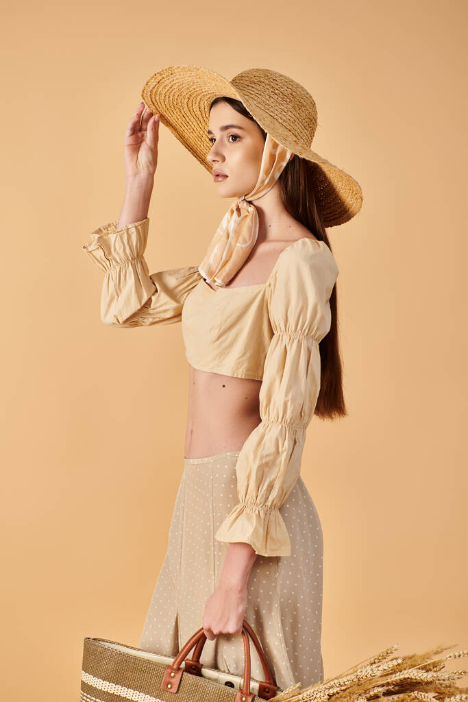 Стильна молода жінка з довгим брюнетка волоссям вражає позу в літньому вбранні, в комплекті з солом'яним капелюхом і сумочкою. - Фото, зображення