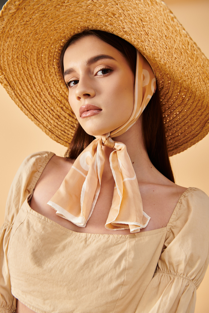 A young woman with long brunette hair strikes a pose in a studio, exuding a summer mood with a straw hat and scarf. - Photo, Image