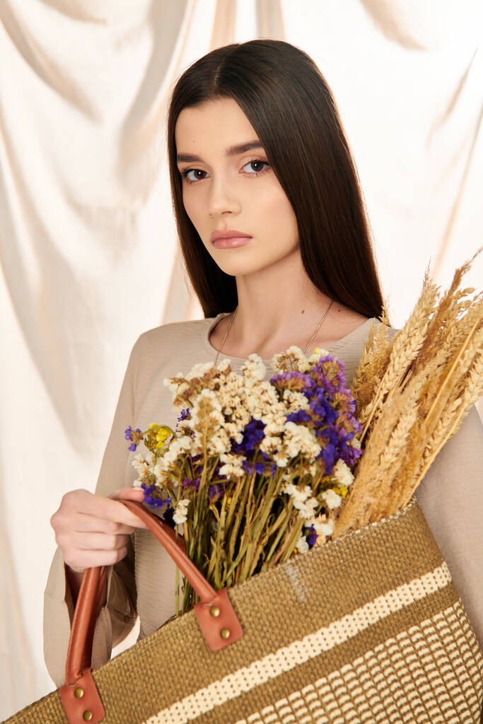 Młoda kobieta z długimi włosami brunetka w letnim stroju trzyma torbę wypełnioną żywymi kwiatami, emanując radosną atmosferą. - Zdjęcie, obraz