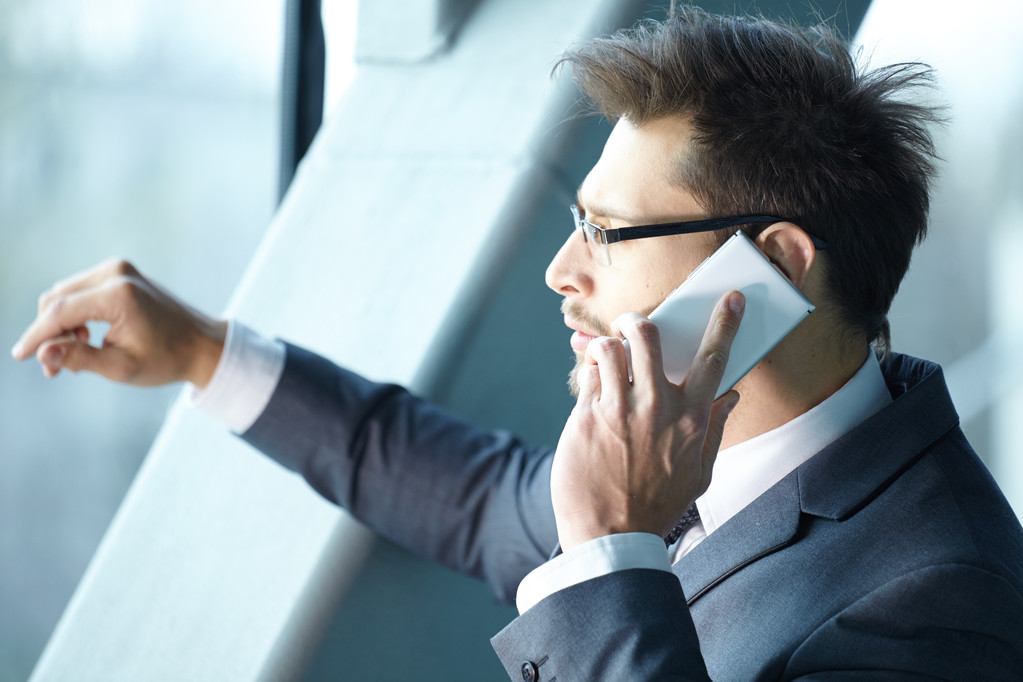 Бизнесмен разговаривает по мобильному телефону в офисном холле
 - Фото, изображение
