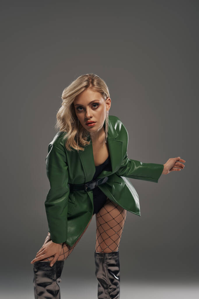 A seductive young woman in a green jacket and fishnet stockings poses alluringly. - Photo, Image