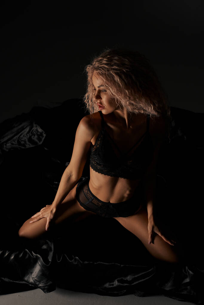 Una mujer seductora en lencería sentada provocativamente en una cama, exudando confianza y encanto. - Foto, Imagen