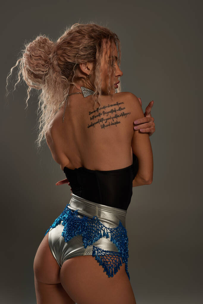Соблазнительная молодая женщина с татуировкой на спине, заманчиво позирующая. - Фото, изображение