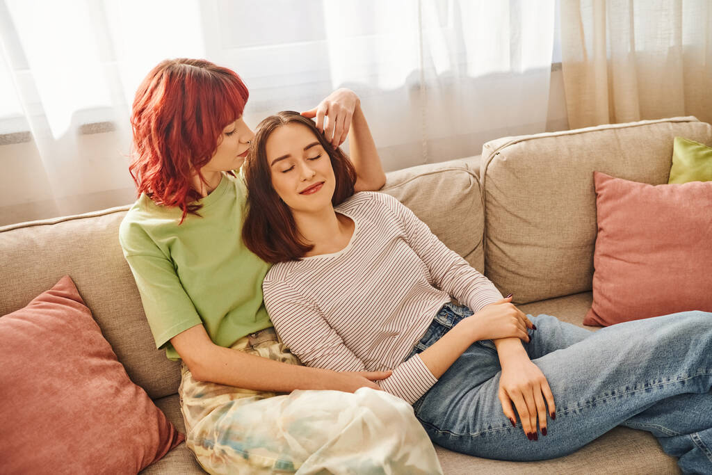 20 'li yaşlarındaki mutlu lezbiyen çift oturma odasındaki kanepede dinlenirken eğleniyor. - Fotoğraf, Görsel