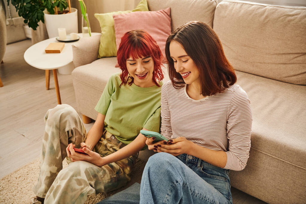 boldog leszbikus pár mosolyog és használja okostelefonok közelében kanapé, modern életmód és a szociális média - Fotó, kép