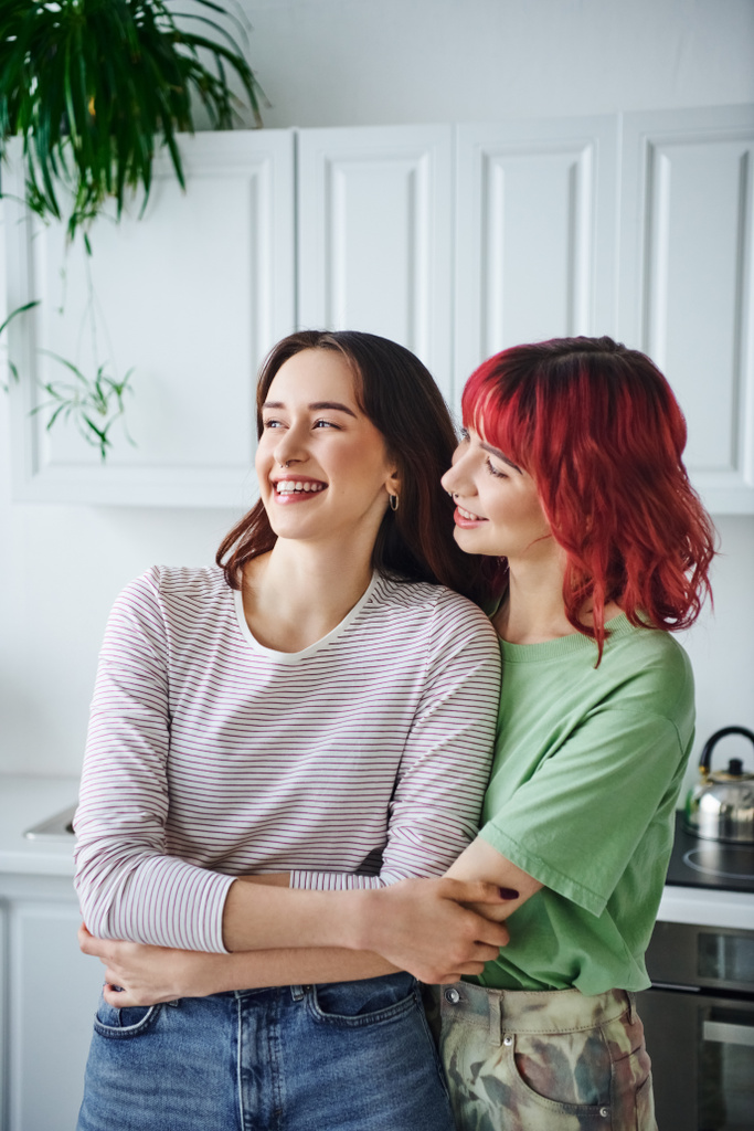 Porträt einer fröhlich durchbohrten lesbischen Frau mit roten Haaren, die ihre Freundin in der Küche anschaut - Foto, Bild