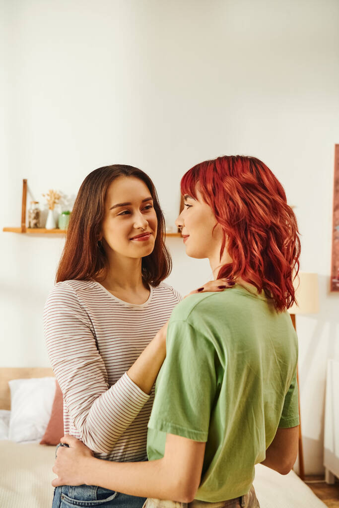 jovem mulher lésbica macia abraçando sua namorada feliz com cabelo vermelho no apartamento moderno - Foto, Imagem