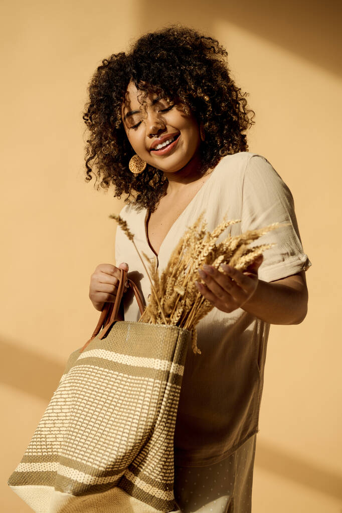 A beautiful young African American woman with curly hair holds a bag filled with wheat, embodying a connection to nature and abundance. - Photo, Image
