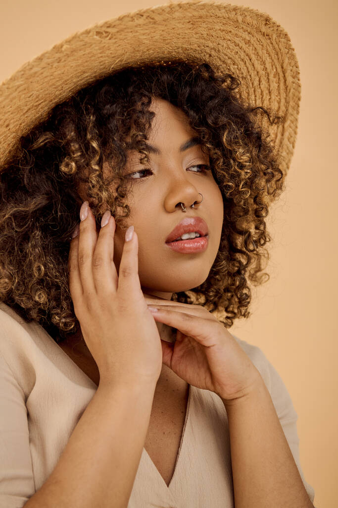 A beautiful young African American woman with curly hair holds her hand to her face, wearing a straw hat and a summer dress. - Photo, Image