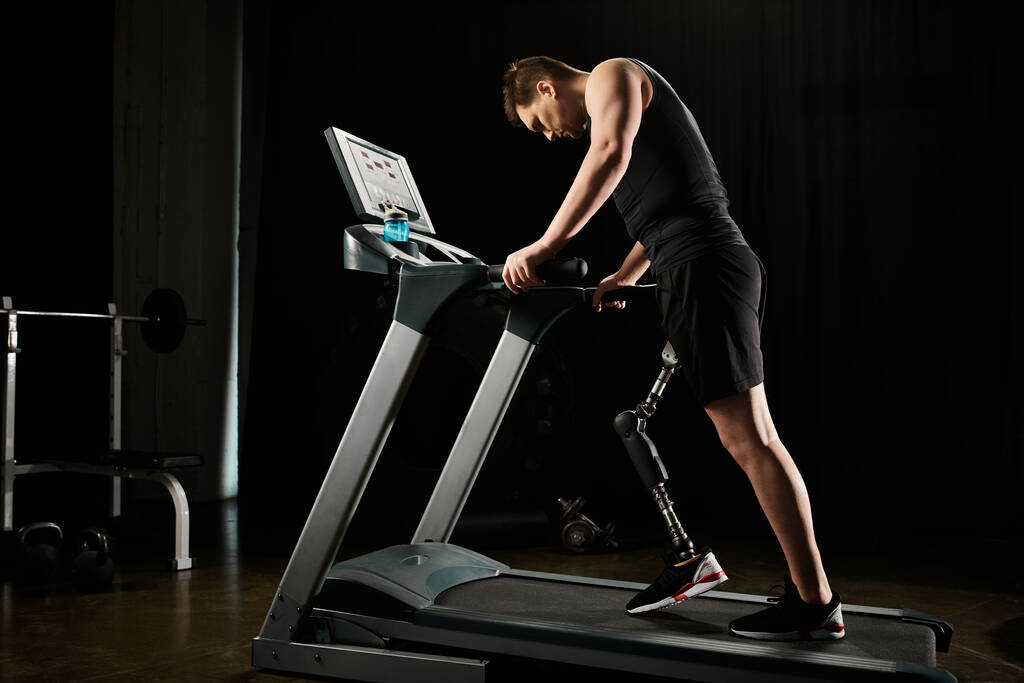 Человек с протезной ногой тренируется на беговой дорожке в темном спортзале - Фото, изображение