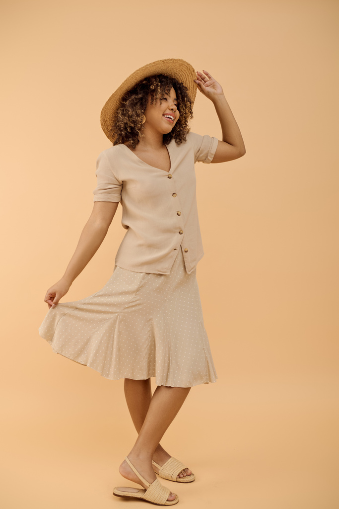Uma mulher afro-americana deslumbrante com cabelo encaracolado, em um vestido de verão e chapéu, marcando uma pose para uma sessão de fotos em um estúdio. - Foto, Imagem