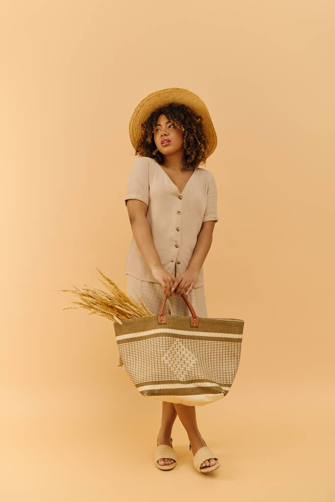 Красива молода афроамериканка з кучерявим волоссям елегантно тримає кошик, прикрашений солом'яним капелюхом і літньою сукнею. - Фото, зображення