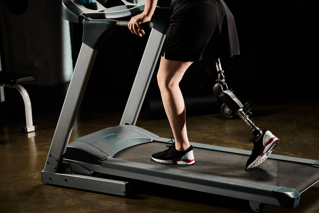 Um homem determinado com uma perna protética está correndo em uma esteira em um ginásio. - Foto, Imagem