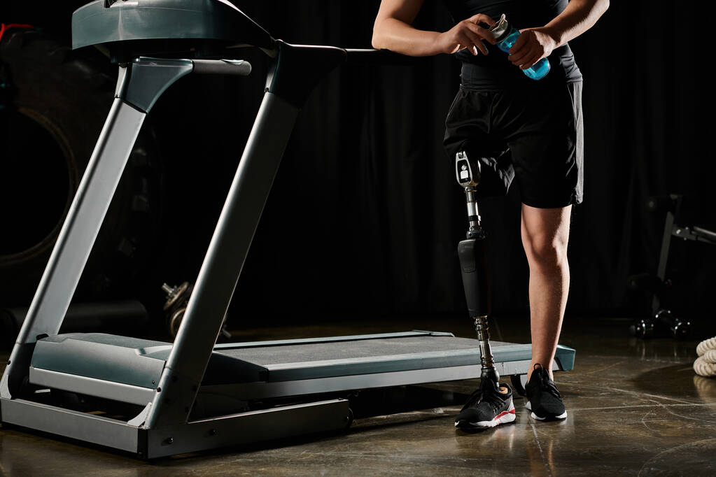 Vammainen mies, jolla on proteesijalka, seisoo juoksumatolla pimeässä huoneessa, keskittyen harjoitusrutiiniinsa.. - Valokuva, kuva