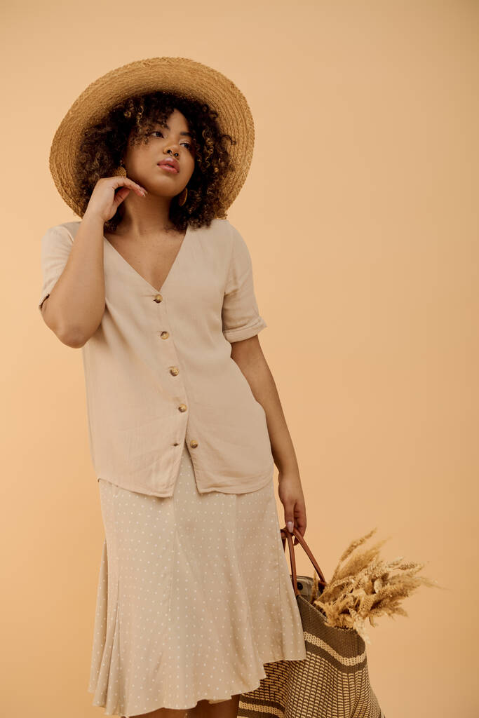 スタイリッシュな若いアフリカ系アメリカ人女性,カーリーヘア,サマードレスと幅広いブリム帽子を着て,バッグを持って. - 写真・画像