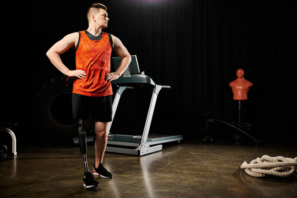 Um homem deficiente com uma perna protética fica confiante na frente de uma esteira em um ginásio, pronto para embarcar em seu treino. - Foto, Imagem