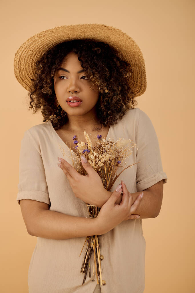 Mladá Afroameričanka s kudrnatými vlasy a letními šaty drží hromadu květin, vyzařující krásu a půvab. - Fotografie, Obrázek
