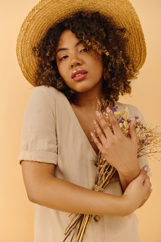 Красивая молодая афроамериканка с вьющимися волосами в соломенной шляпе, держащая в руках букет разноцветных цветов. - Фото, изображение