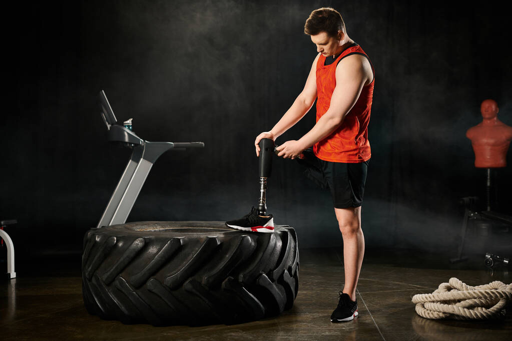 Ein behinderter Mann mit Beinprothese steht neben einem Reifen auf einem Tisch und zeigt Kraft und Gleichgewicht. - Foto, Bild